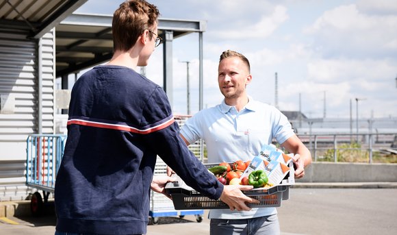 Ein DB-Mitarbeiter übergibt einen Korb mit Lebensmittelspenden an einen Mitarbeiter der Tafel. 